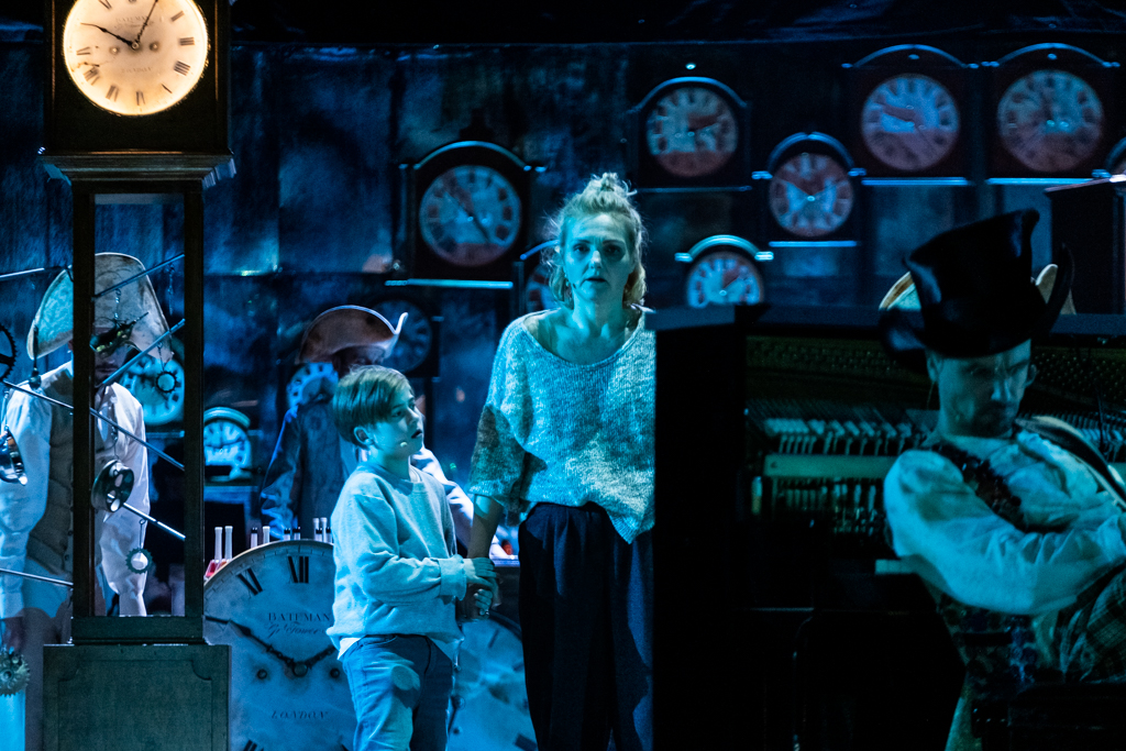 Alicja wraz z małym chłopcem znajduje się w otoczeniu zegarów. Przed nią widać Kapelusznika, który gra na pianinie. Alicja zastanawia się nad czymś.