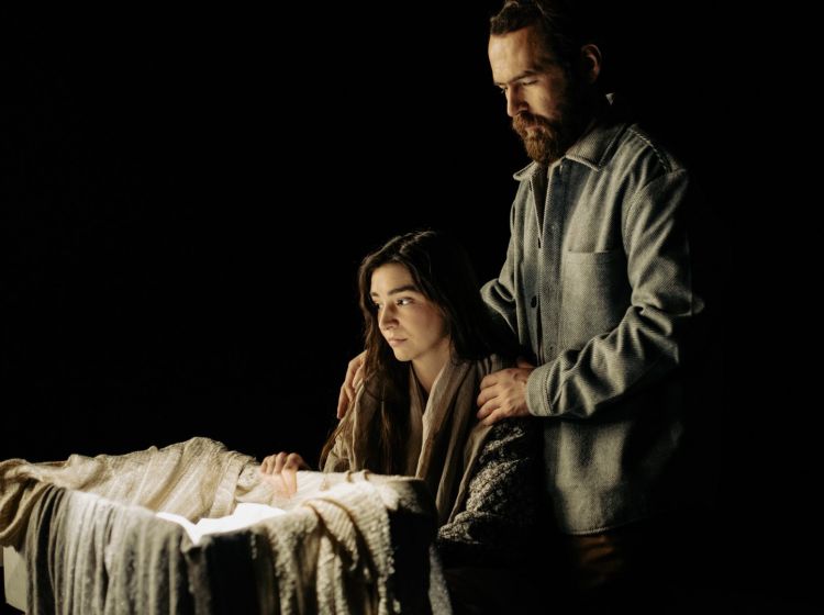 Mężczyzna trzyma dłonie na ramionach siedzącej kobiety siedzącej przy kołysce.