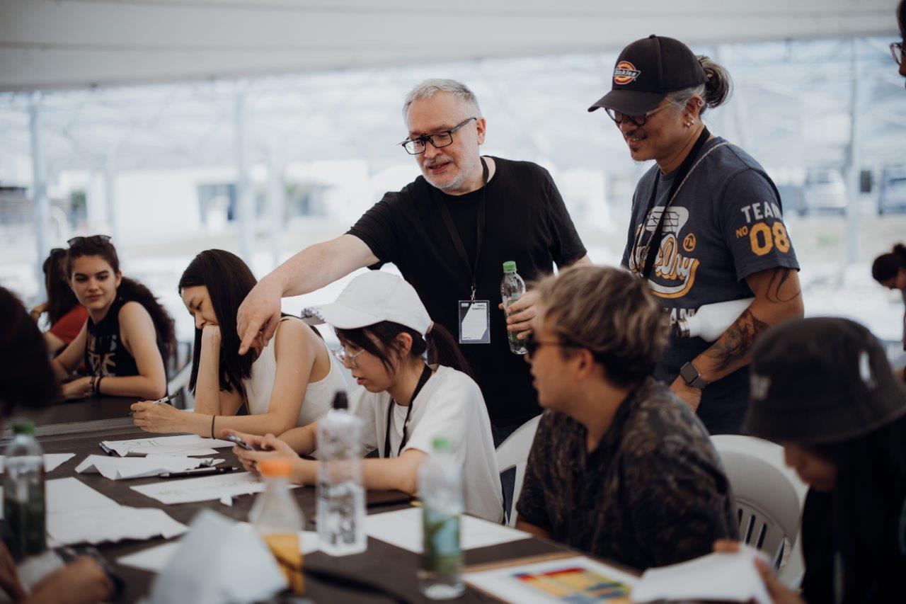 Stojący mężczyzna omawia prace siedzących przy stole studentów