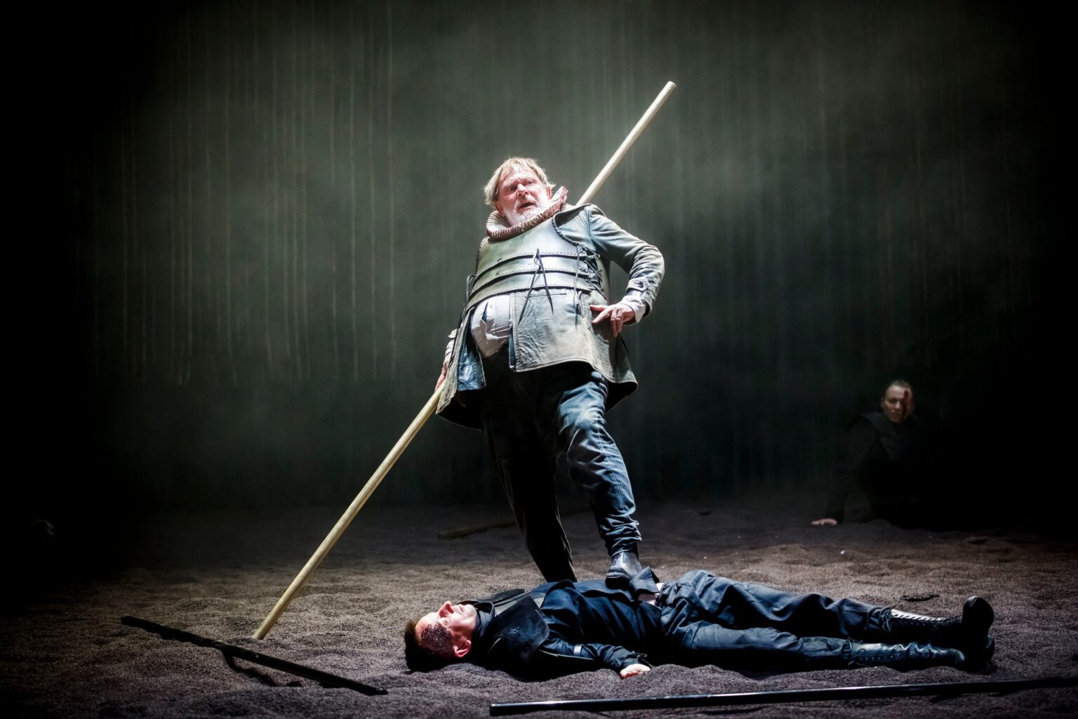 Zdjęcie przedstawiające aktora ubranego w srebrną zbroję, trzymającego nogę na klatce leżącego aktora ubranego w historyczny kostium