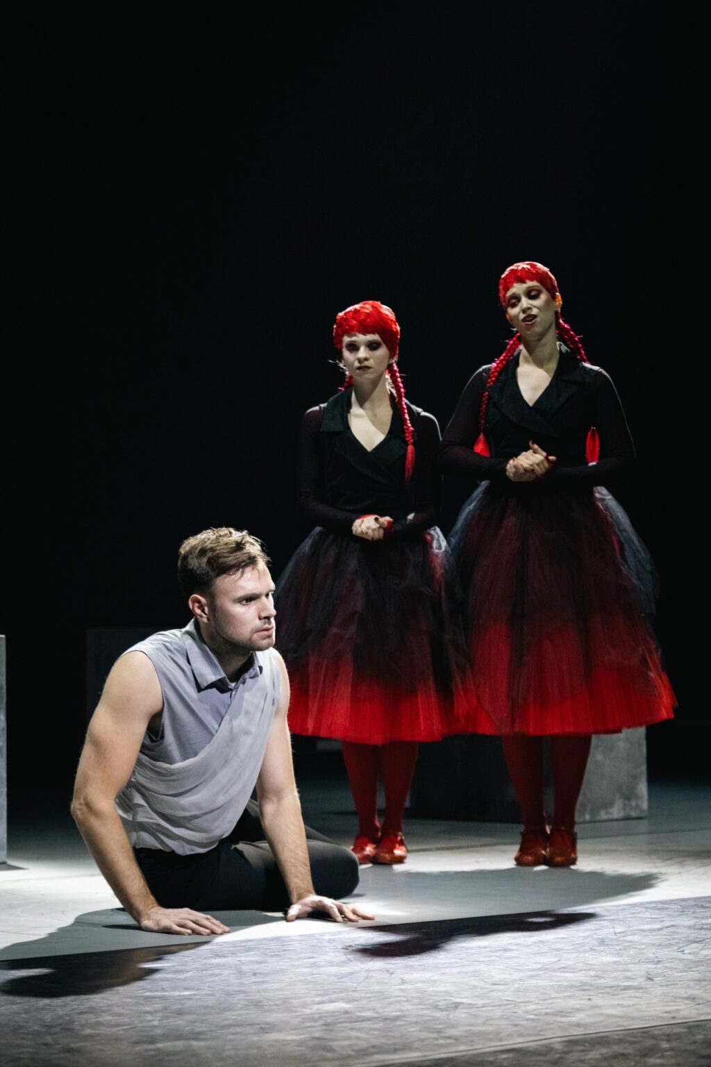 dwie identycznie ubrane ubrane w czarno-czerwone stroje kobiety oraz mężczyzna siedzący na ziemi