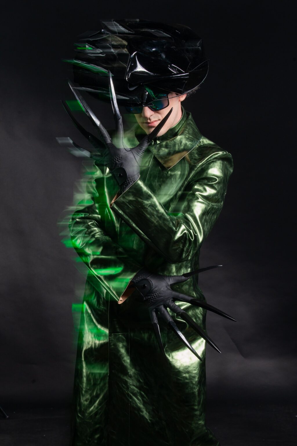 Mężczyzna ubrany w zielny, mieniący się skórzany płaszcz. Na ręku ma rękawiczkę z bardzo długimi pazurami.