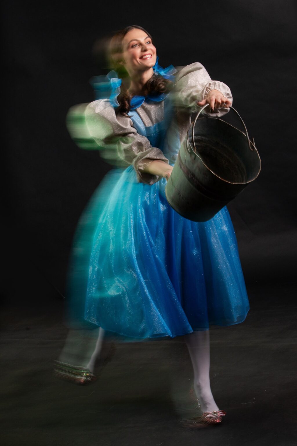 Kobieta ubrana w niebiesko-białą sukienkę, trzymająca wiadro w ręku