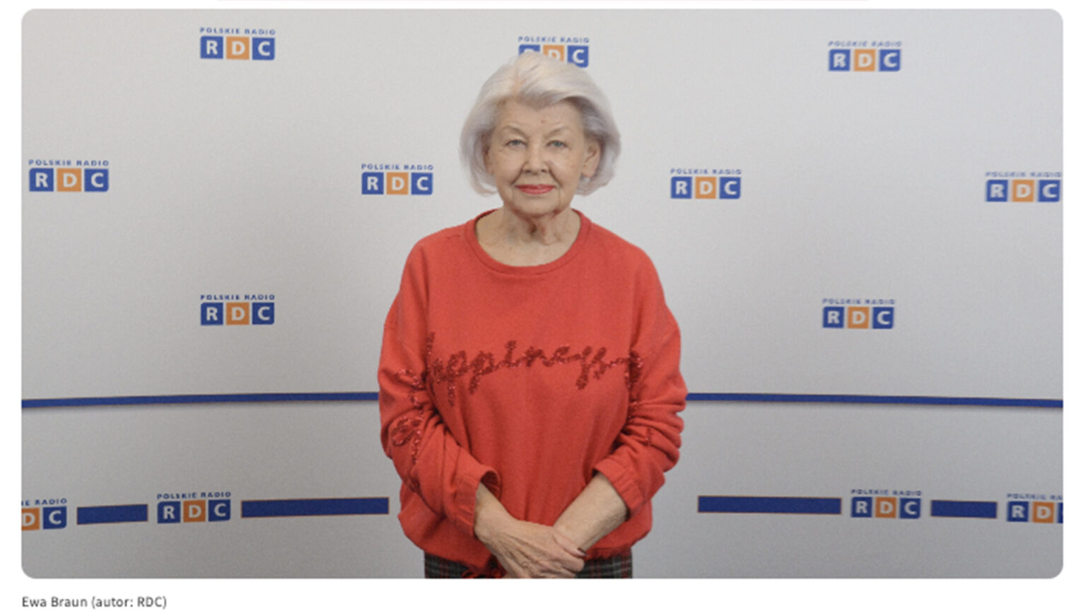 Zdjęcie prof. Ewy Braun na tle ścianki z logiem RDC. Kobieta ubrana jest w czerwoną bluzkę.