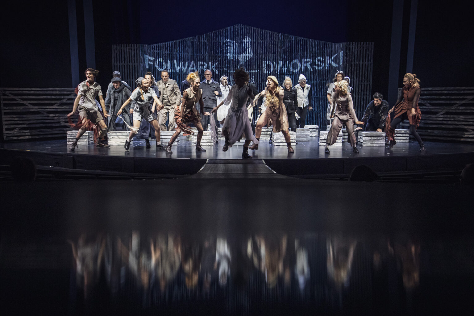 Zdjęcie ze spektaklu Folwark zwierzęcy, przedstawiający grupę ludzi ubranych w kostiumy inspirowane latami 60 w Polsce.