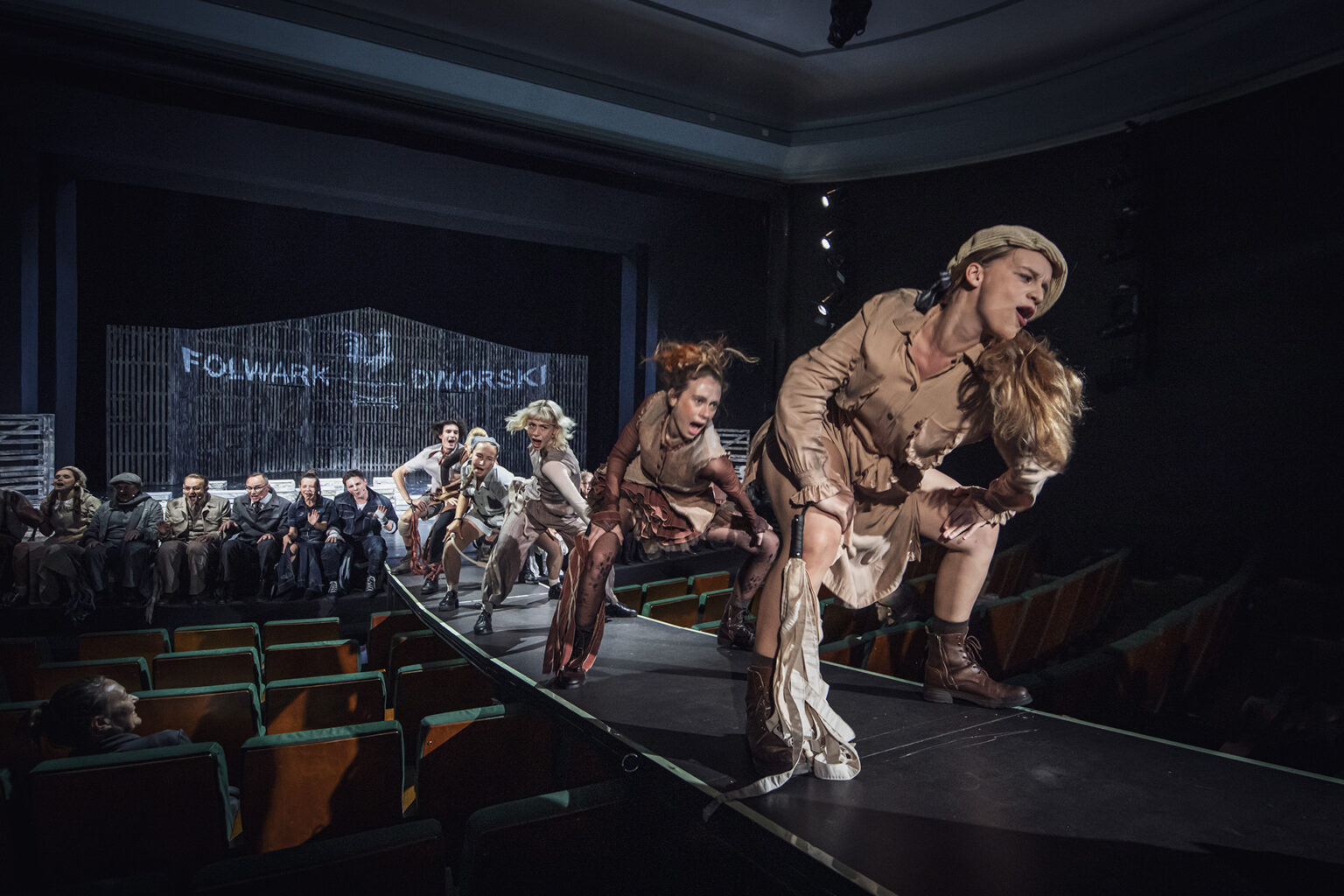 Zdjęcie ze spektaklu Folwark zwierzęcy, przedstawiający grupę ludzi ubranych w kostiumy inspirowane latami 60 w Polsce.