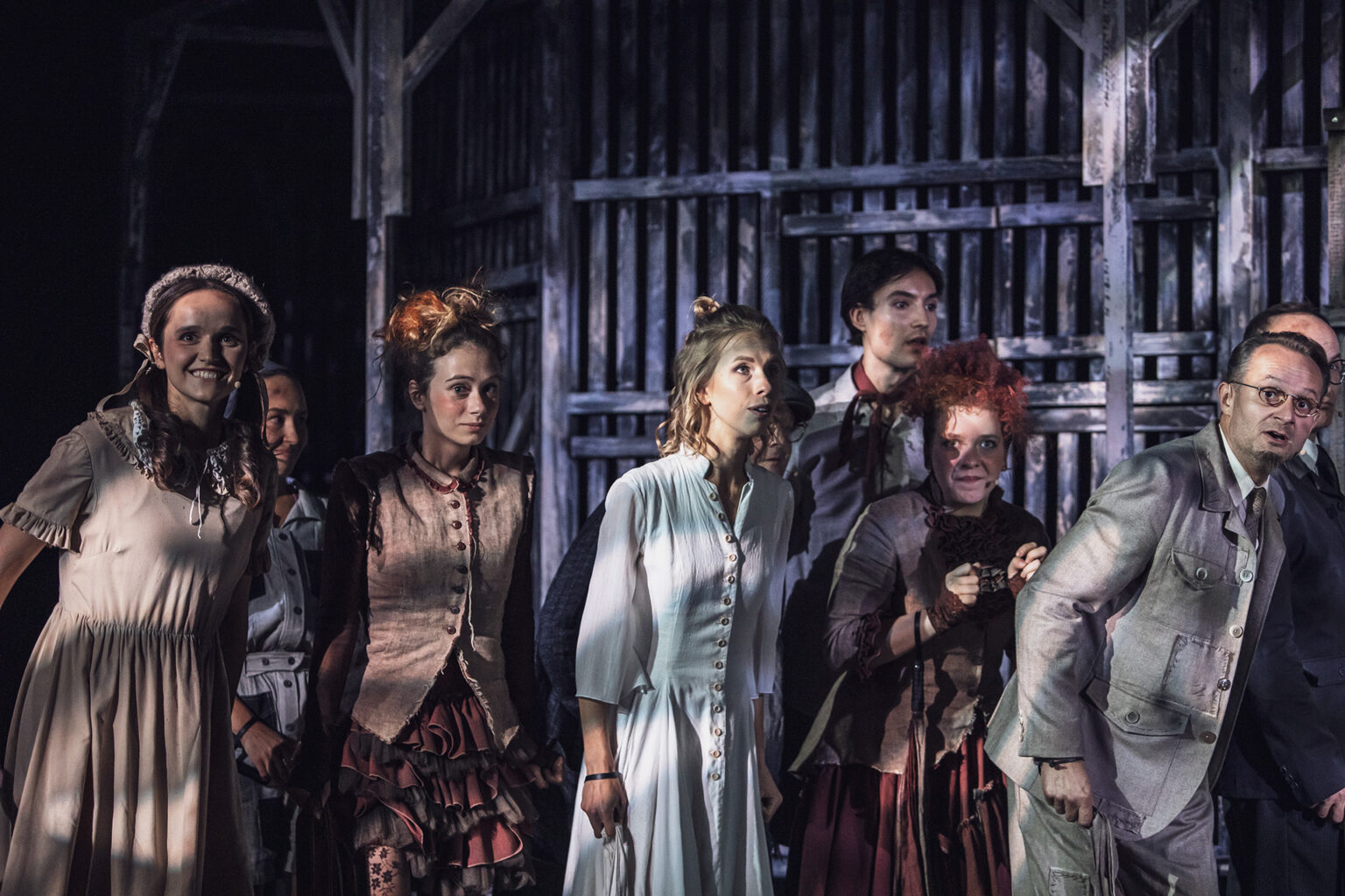 Zdjęcie ze spektaklu Folwark zwierzęcy, przedstawiający grupę ludzi ubranych w kostiumy inspirowane latami 60 w Polsce.