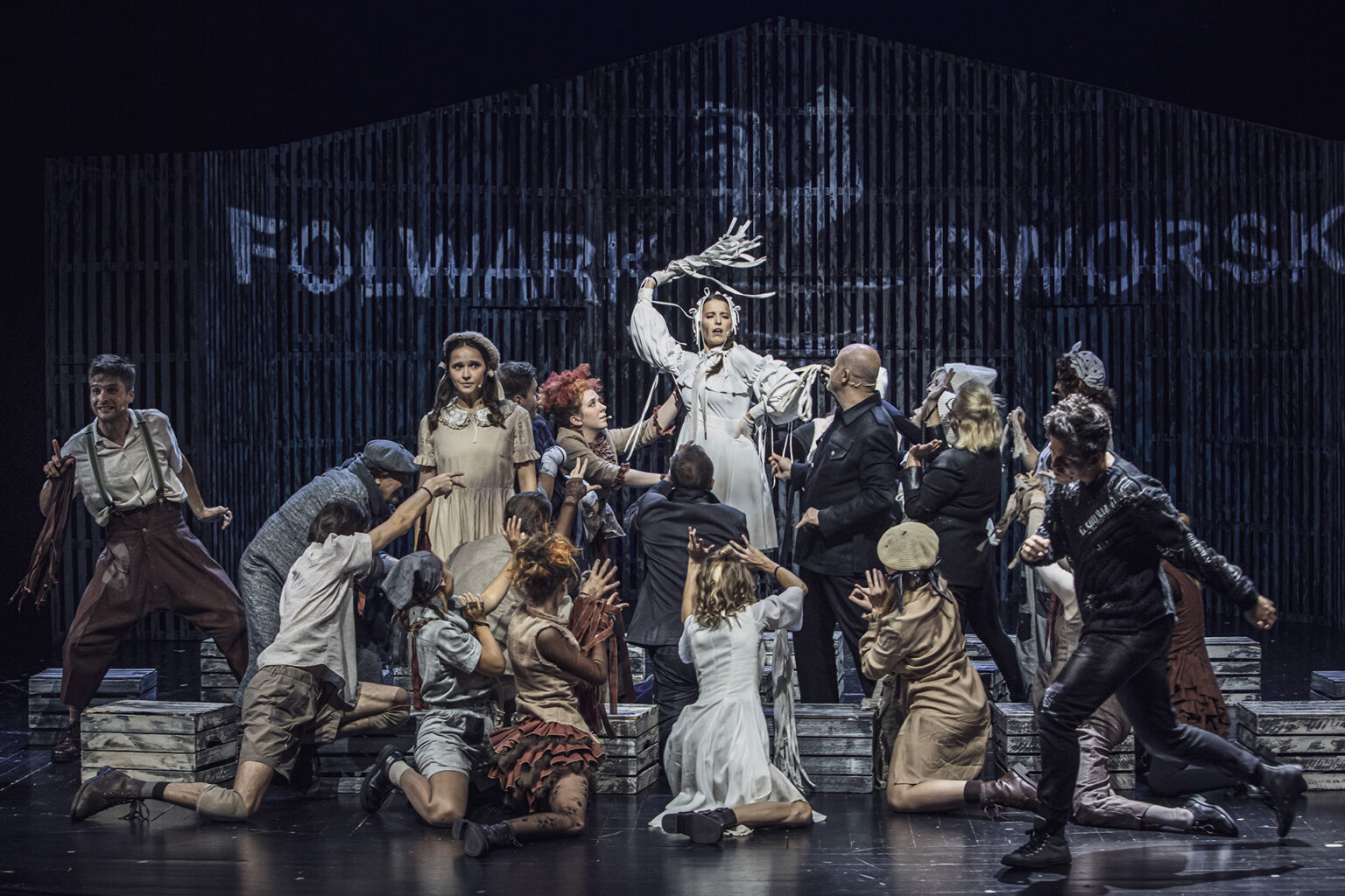 Zdjęcie ze spektaklu Folwark zwierzęcy, przedstawiający grupę ludzi ubranych w kostiumy inspirowane latami 60 w Polsce.