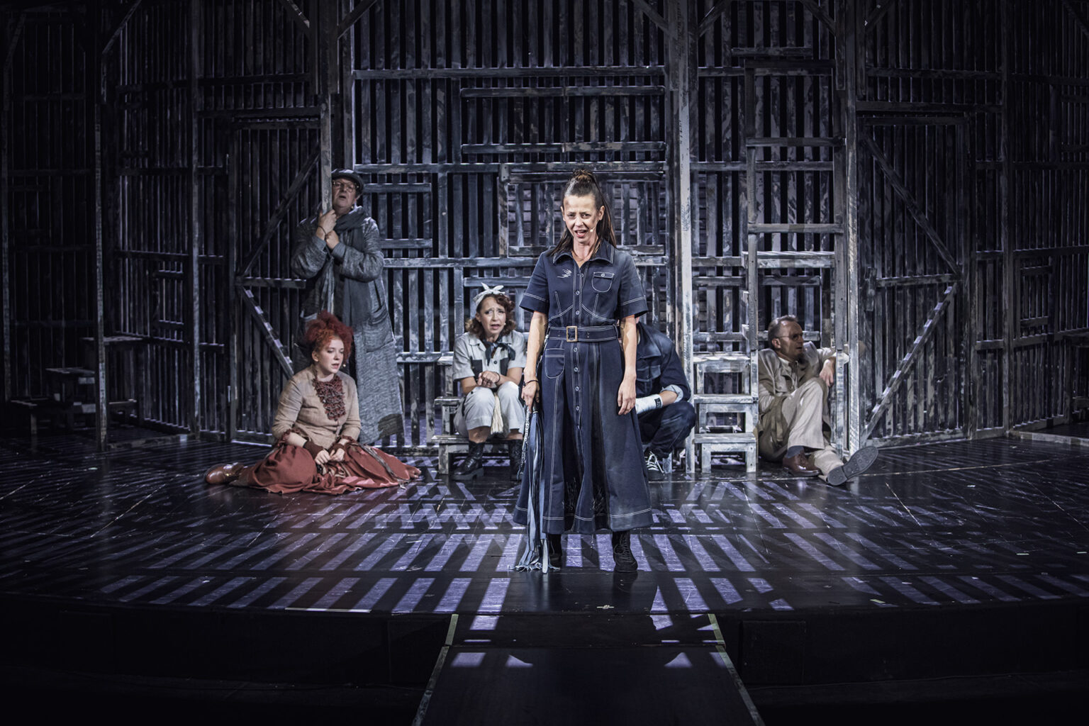 Zdjęcie ze spektaklu Folwark zwierzęcy, przedstawiający grupę ludzi ubranych w kostiumy inspirowane latami 60 w Polsce.