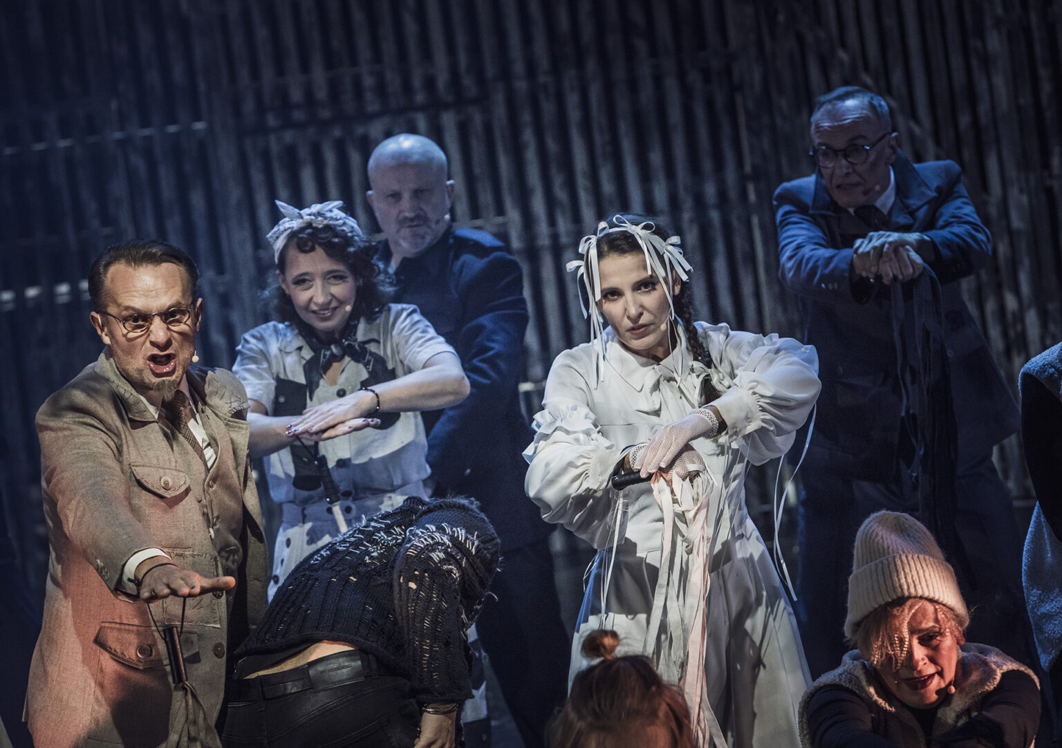 Zdjęcie ze spektaklu Folwark zwierzęcy, przedstawiający grupę ludzi ubranych w kostiumy inspirowane latami 60 w Polsce.