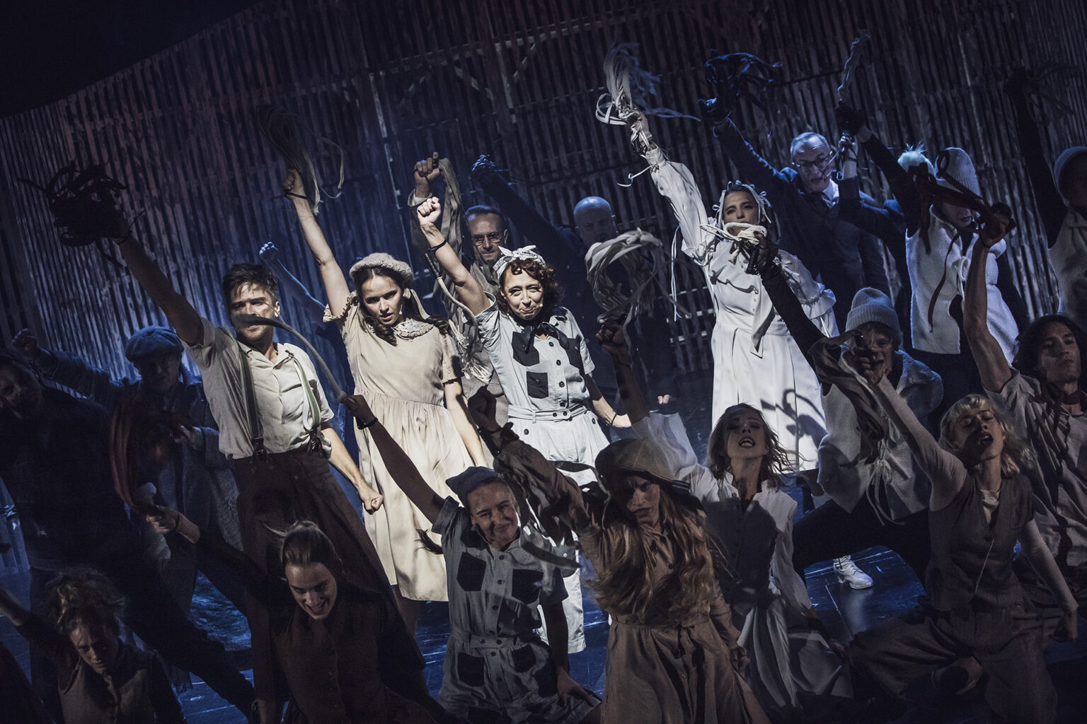 Zdjęcie ze spektaklu Folwark zwierzęcy, przedstawiający grupę ludzi ubranych w kostiumy inspirowane latami 60 w Polsce.