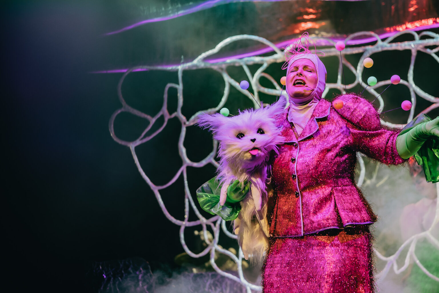 Śpiewająca kobieta w różowej garsonce, trzymająca dużego sztucznego kota.