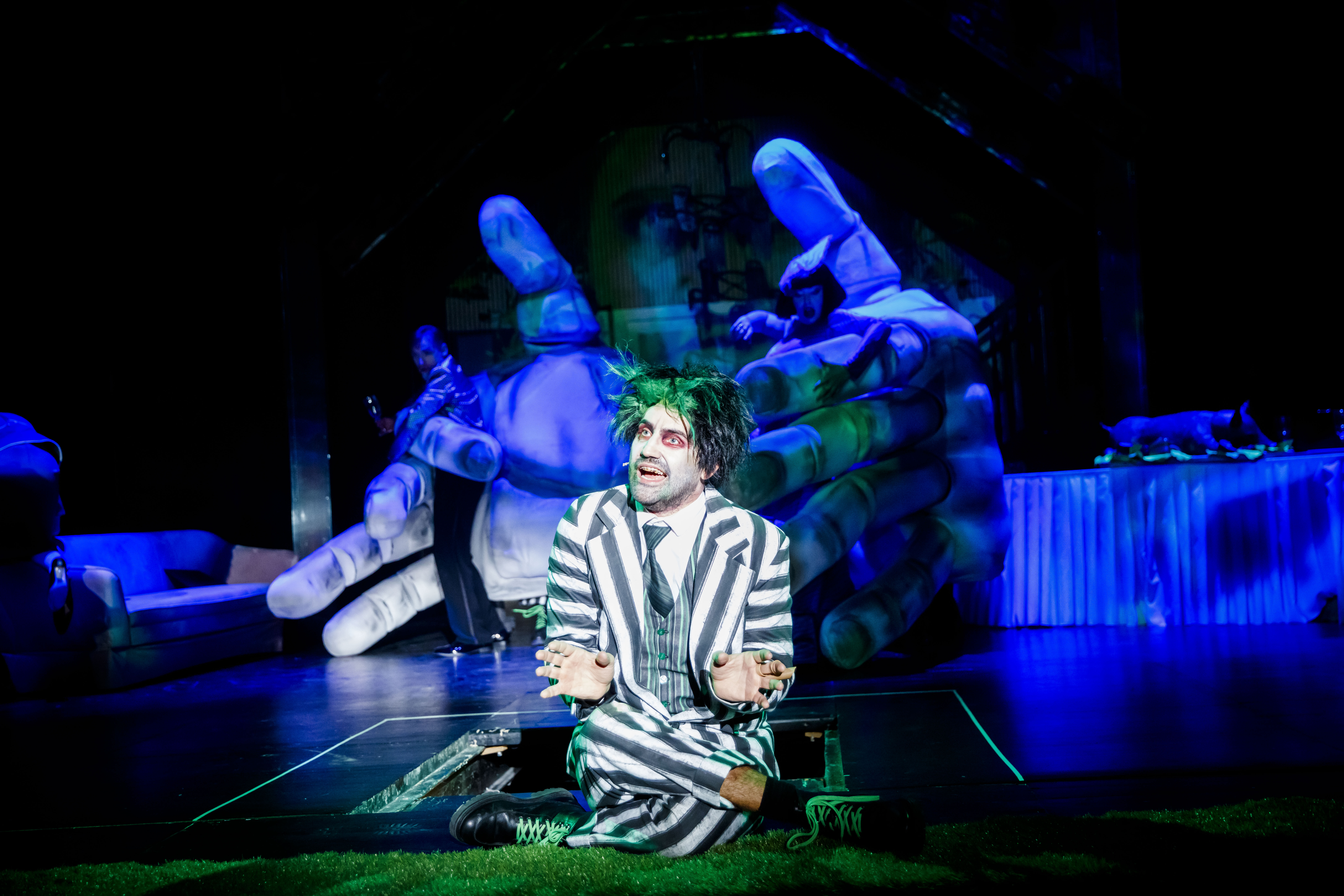 Mężczyzna w garniturze w paski, sfotografowany na tle gigantycznych rąk.