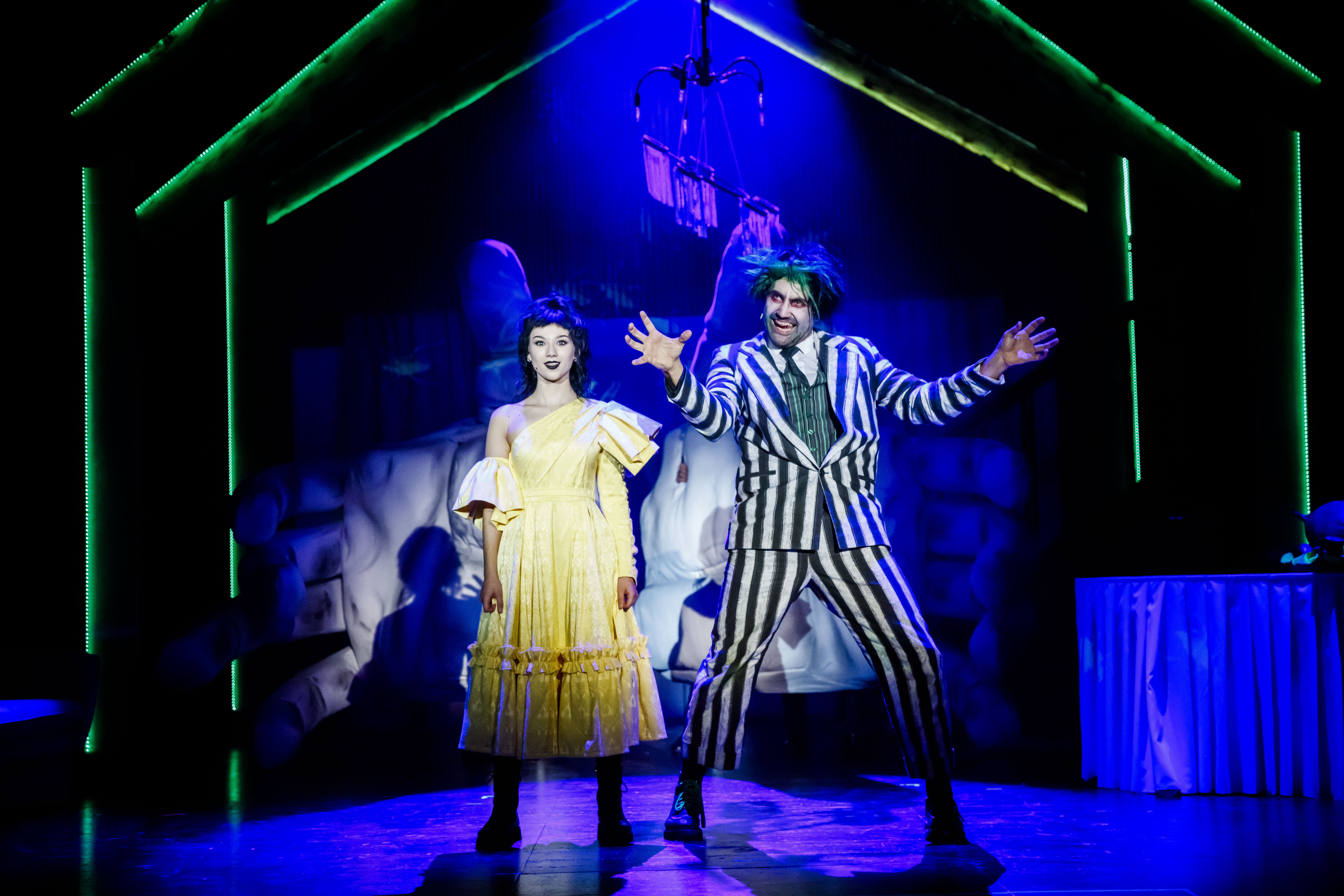 Zdjęcie młodej kobiety w żółtej sukience oraz mężczyzny w garniturze w paski na tle gigantycznych dłoni.