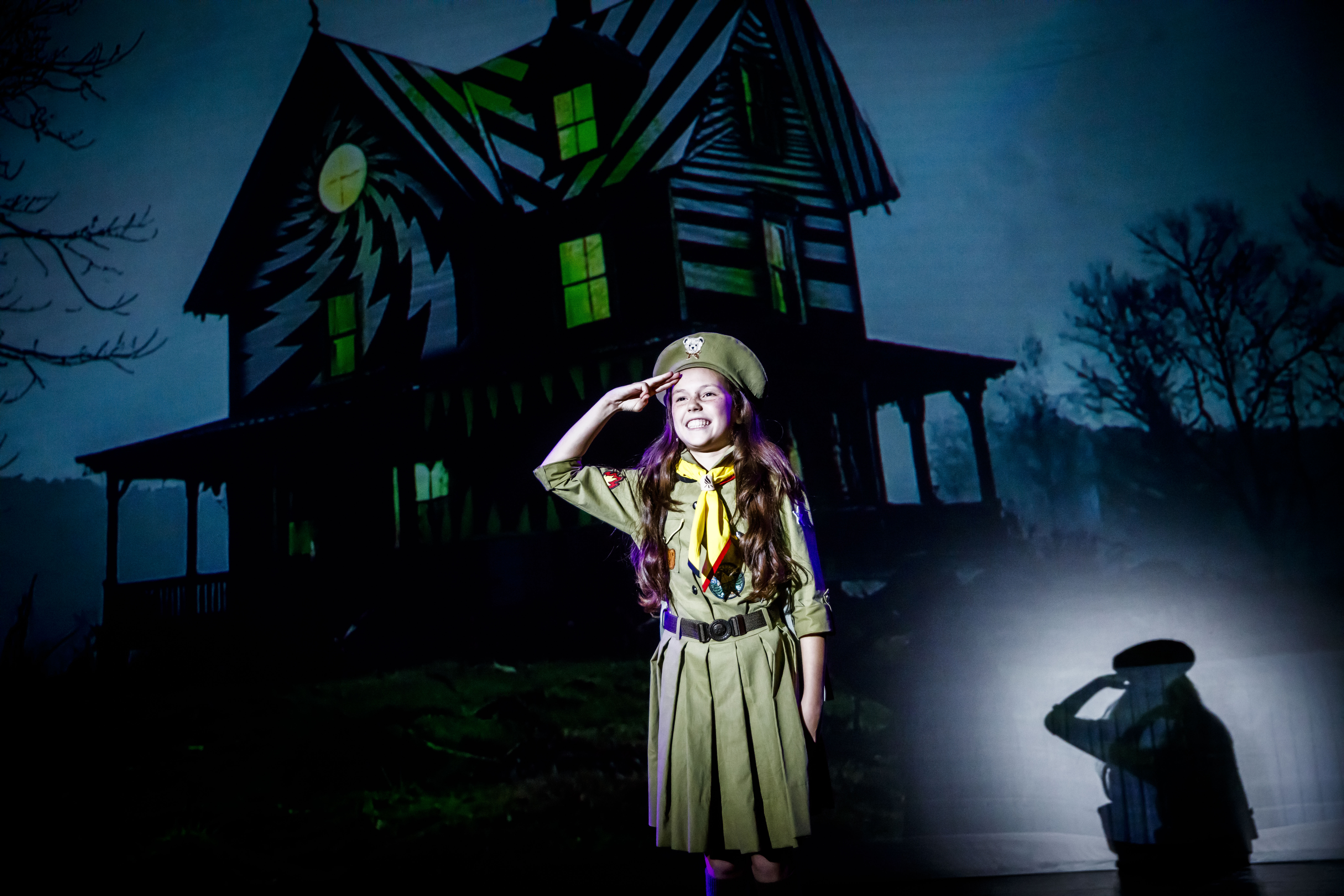 Zdjęcie małej harcerki na tle ekranu, na których wyświetlony jest domek.