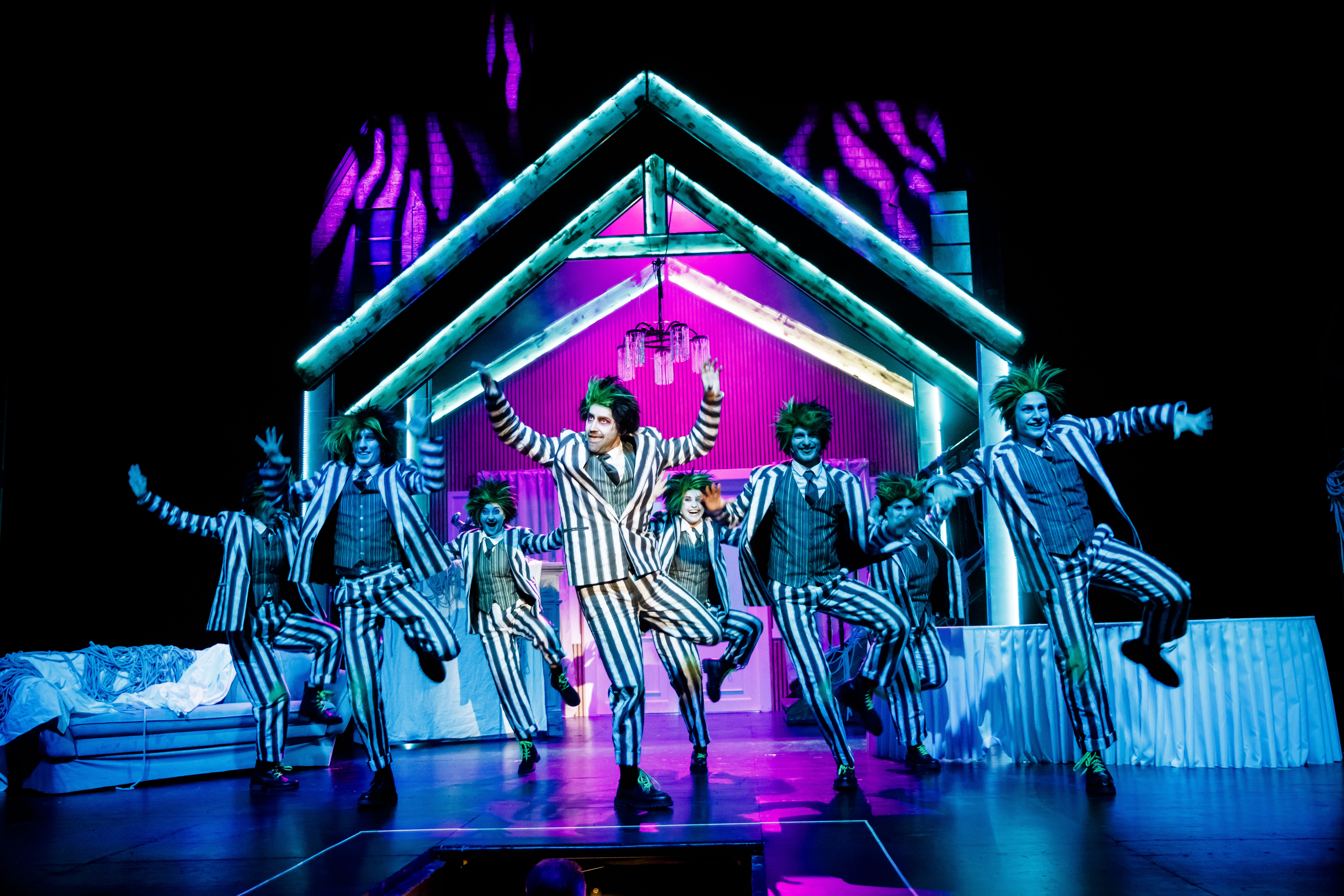 zdjęcie grupy osób ubranych w garnitury w paski, tańczących na tle domku.