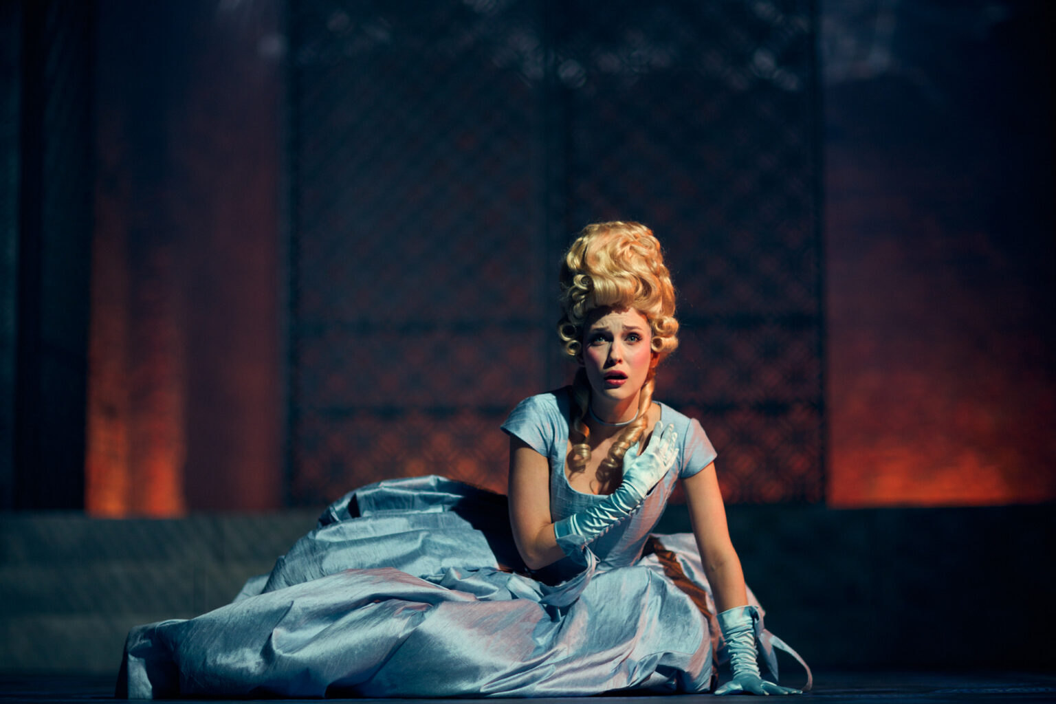 Kobieta w błękitnej sukience, leży na podłodze. Widać, że jest czymś przejęta.