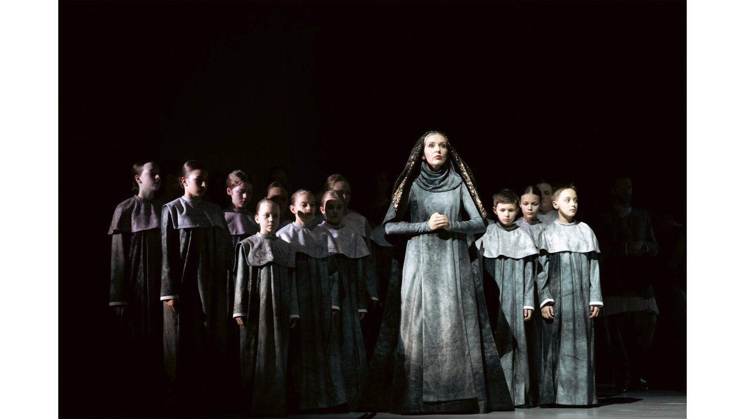 Zdjęcie przedstawia zakonnice, na której tle stoją dzieci. Wszyscy ubrani są w kostiumy strukturą przypominającą kamień.